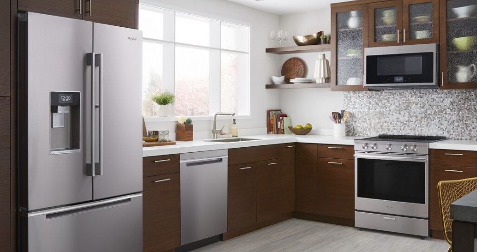 Whirlpool Combination Microwave Une cuisine avec un réfrigérateur Whirlpool, un lave-vaisselle Whirlpool, un four à micro-ondes Whirlpool et un four Whirlpool. Dans la cuisine se trouvent également une table et une chaise, des étagères avec des bols et une planche à découper, un bol de fruits et une plante en pot